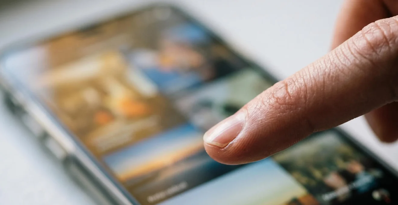 Close-up of a finger pausing mid-scroll over a smartphone screen showing video thumbnails, captured at eye-level with shallow depth of field