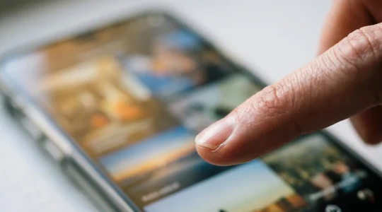 Close-up of a finger pausing mid-scroll over a smartphone screen showing video thumbnails, captured at eye-level with shallow depth of field